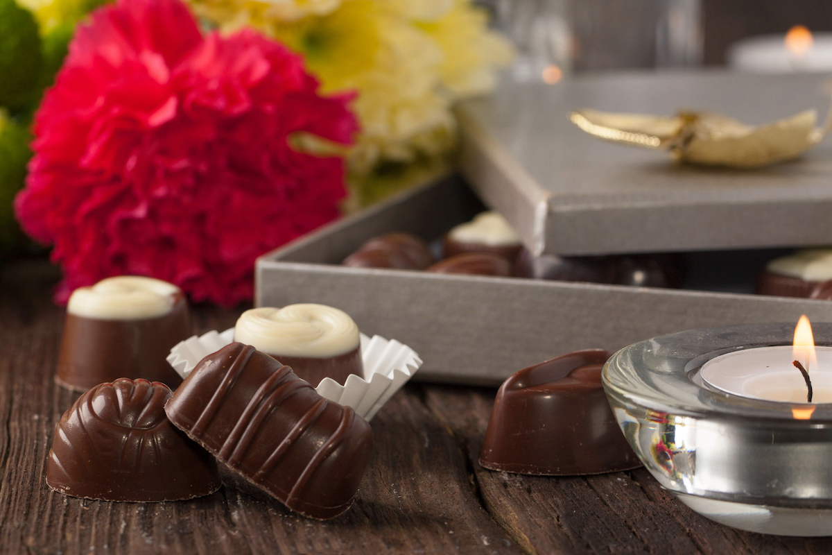 Chocolate candies, lightning candle and bouquet of carnation and chrysanthemum flowers on old wooden table